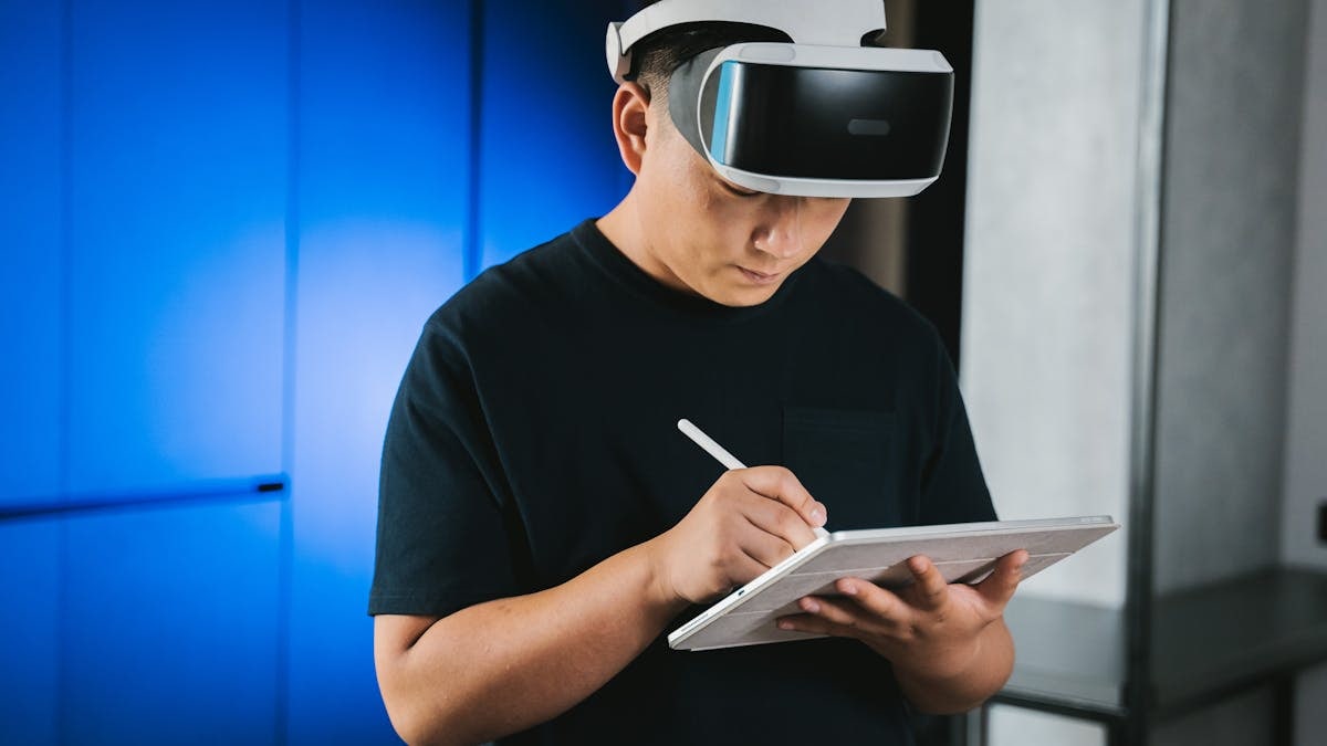 A man indoors wearing a VR headset while writing on a tablet with a stylus pen.