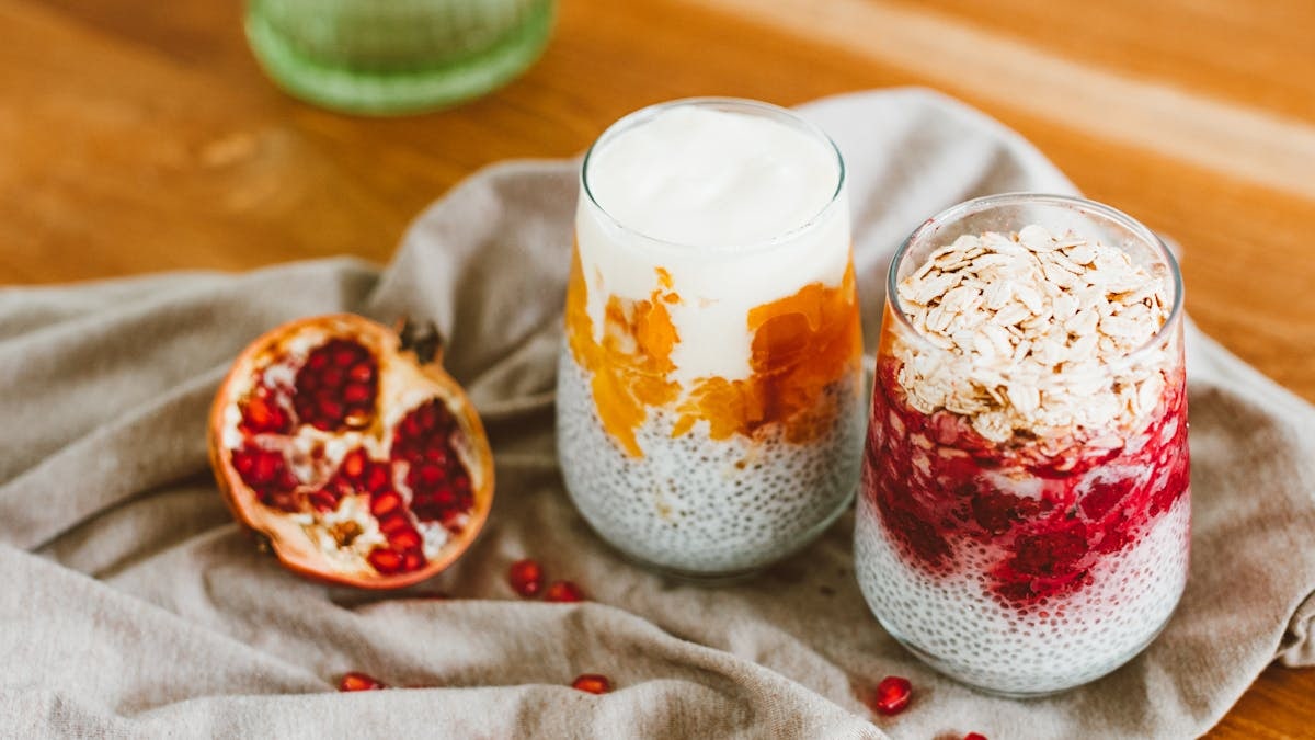 Two chia seed parfaits with yogurt, pomegranate, and oats on a wooden table.